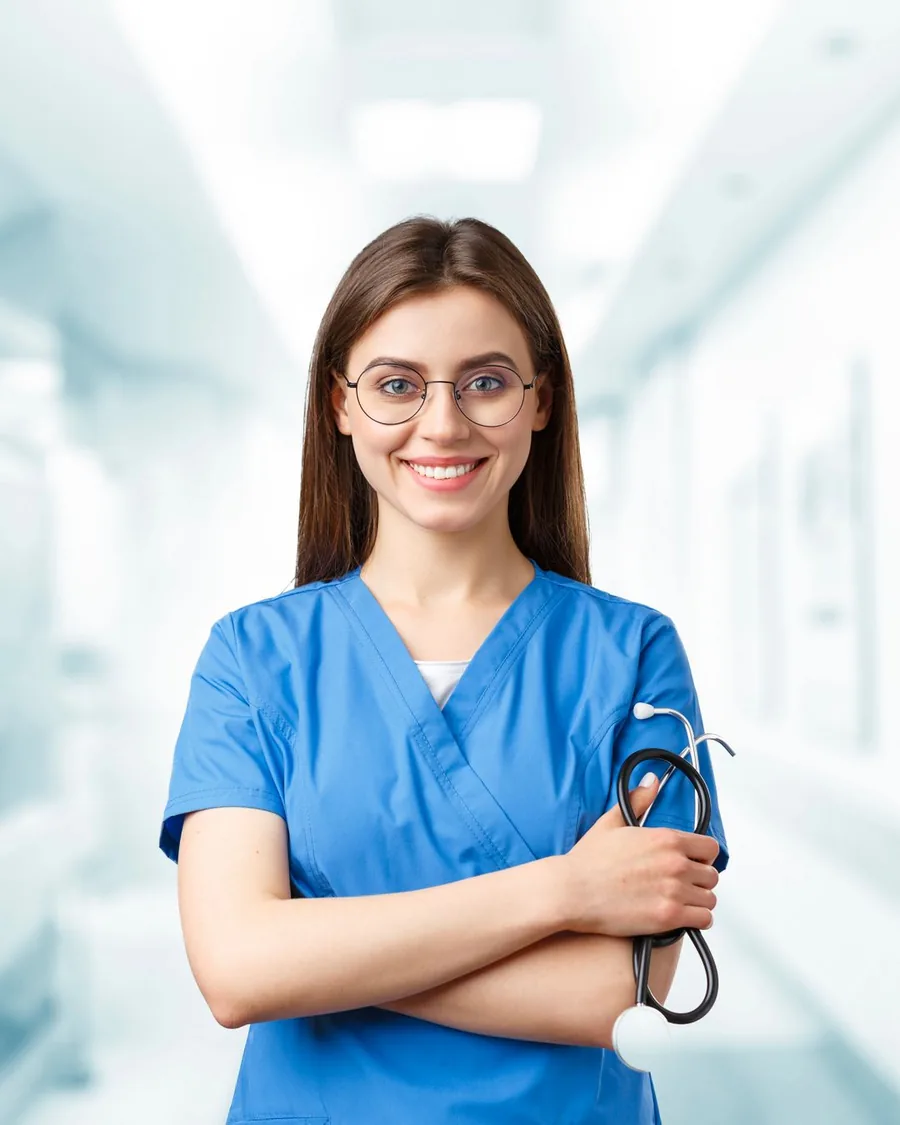 A nurse in scrubs standing with a stethoscope in a bright clinical corridor