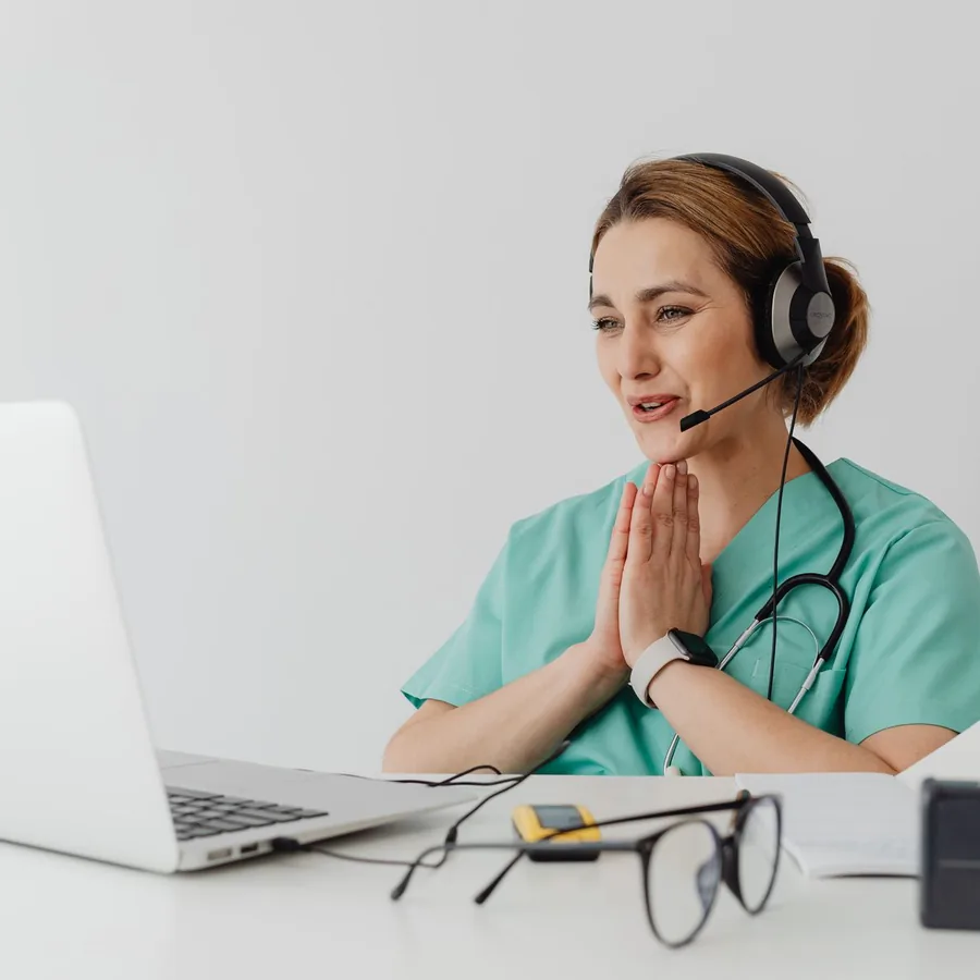 A nurse at a workstation wearing a headset, speaking during a phone consultation
