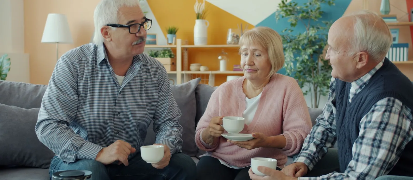 Three older adults sitting together over coffee in a bright, comfortable living room